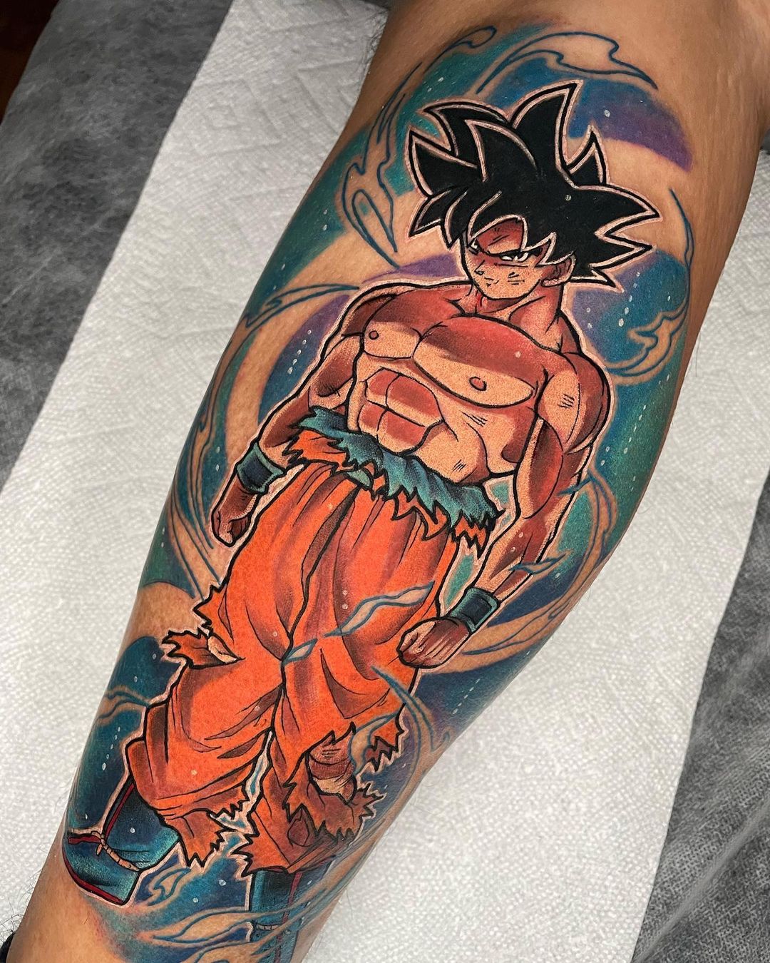 this tattoo features goku surrounded in the power and godhood of ultra instict omen