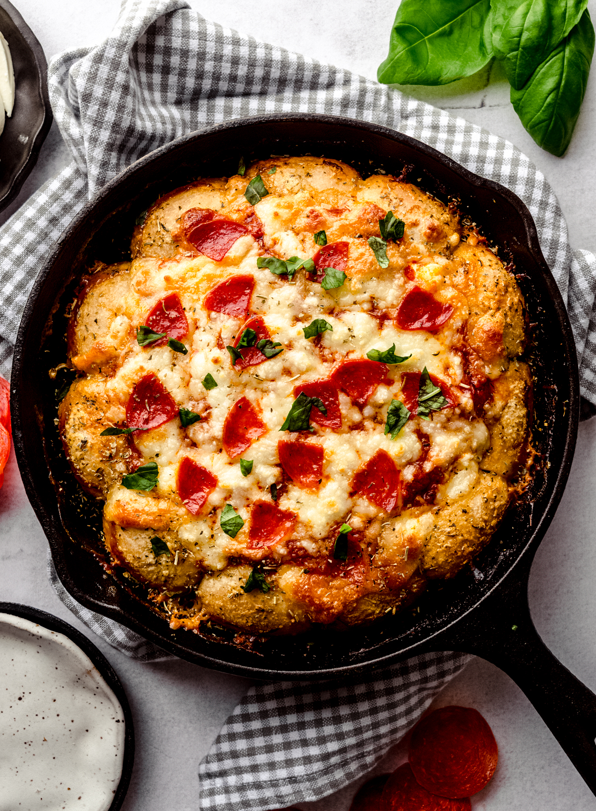 An aerial photo of a skillet of pizza dip on a gray and white checkered towel.