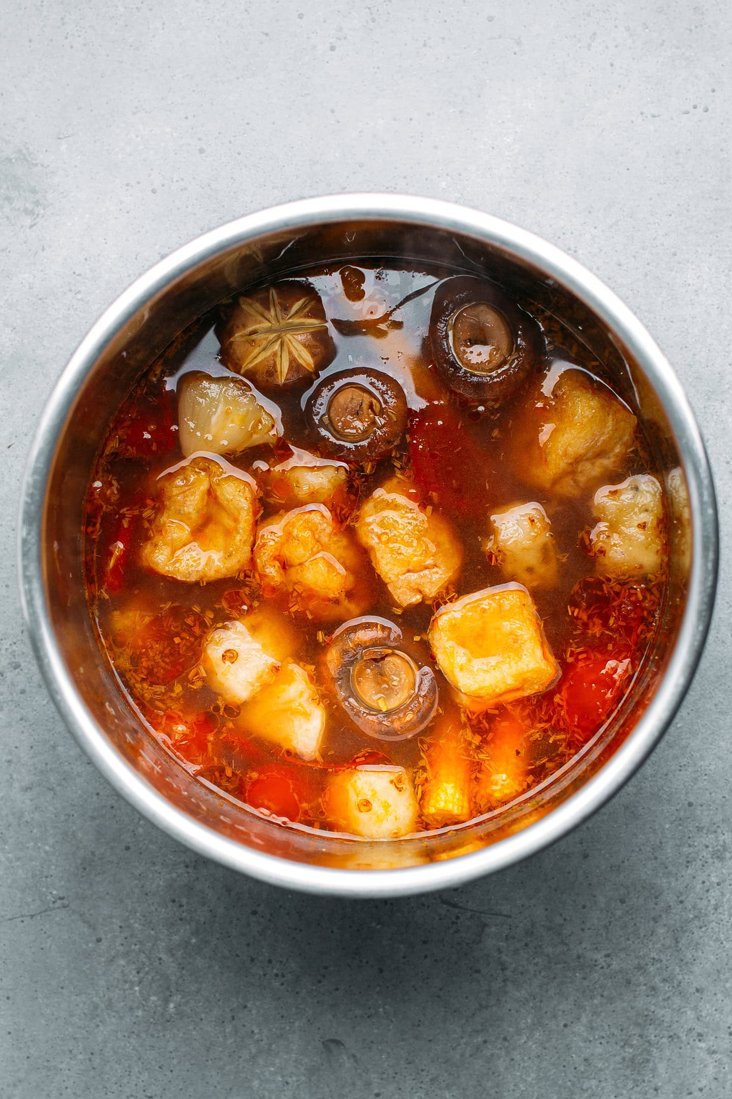 Spicy broth with tofu, mushrooms, and tomatoes in a pot.