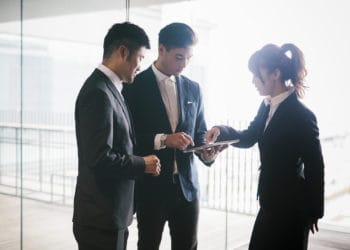 Three co-workers hold a business meeting in a bright office demonstrating the latest technological solutions.