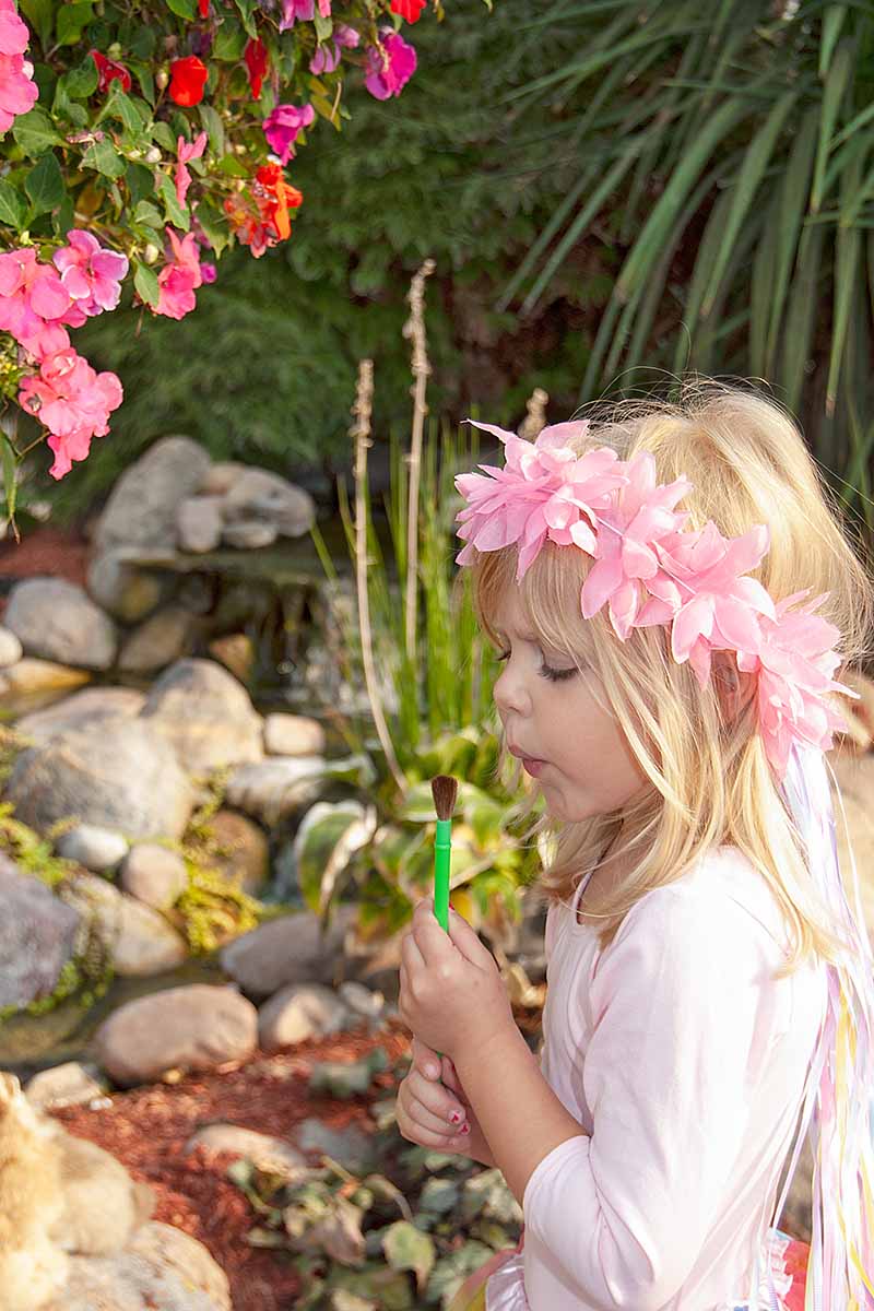 A close up vertical image of a young girl dressed as a fairy in a rock garden.