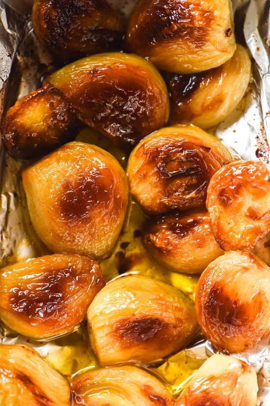 An aerial macro image of low FODMAP roasted garlic pieces in oil and tin foil.