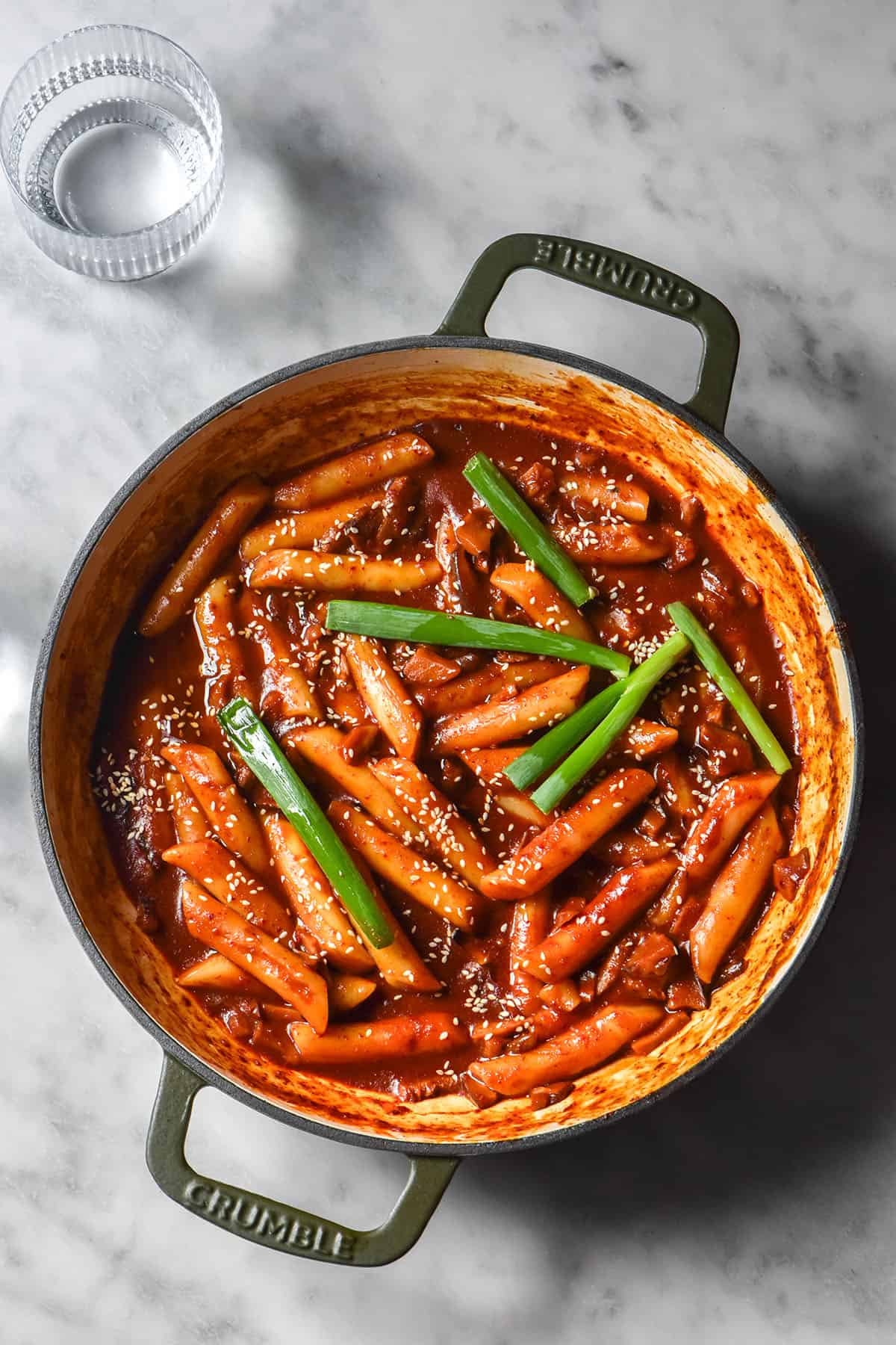 An aerial image of a skillet filled with vegan gluten free tteokbokki on a white marble table.