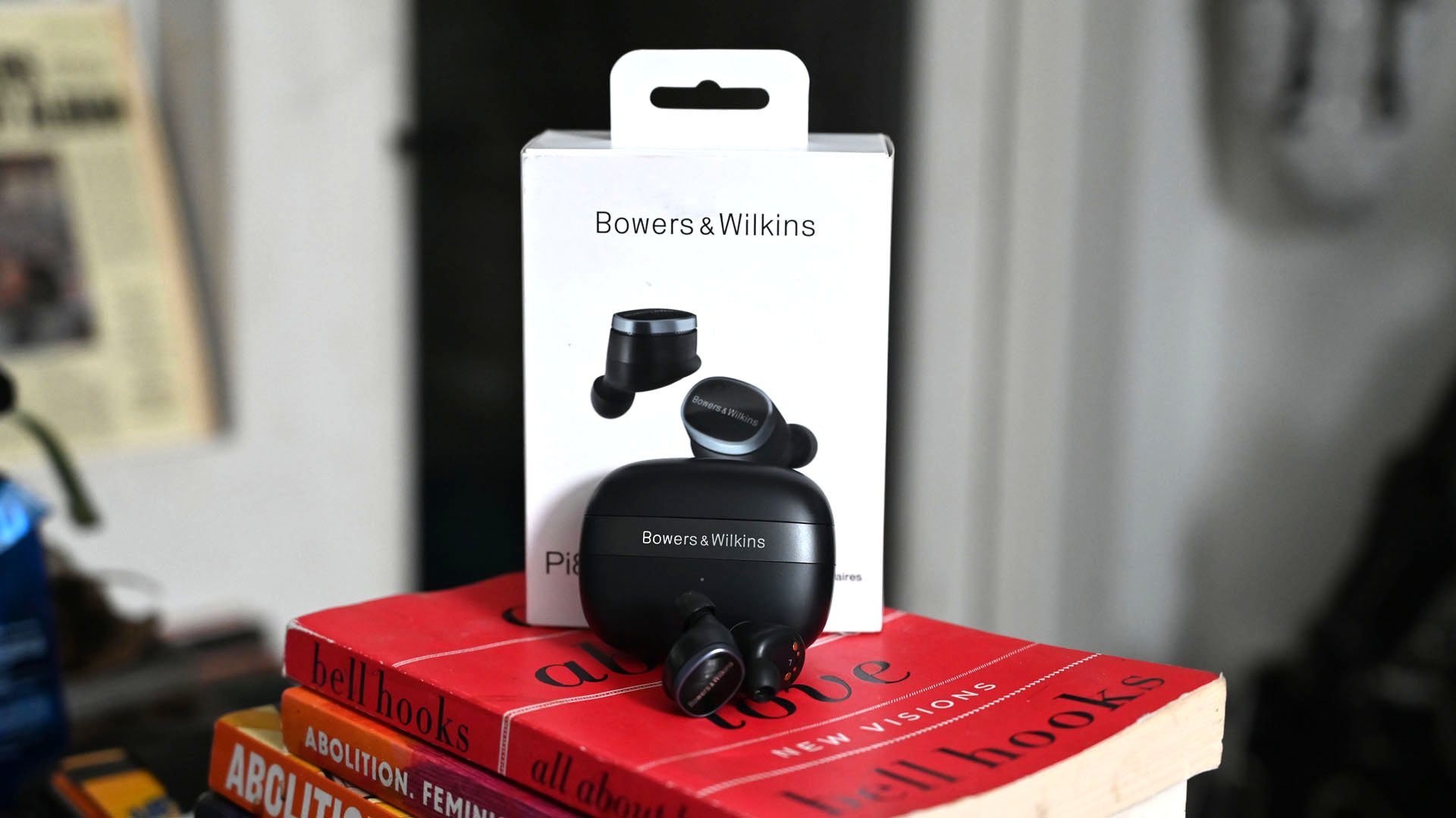 Shot of Bowers & Wilkins Pi8 earbuds with charging case and box on top of red book.