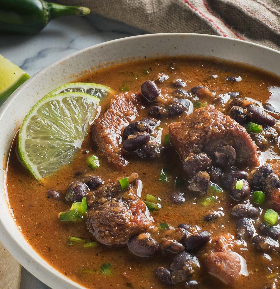 Close up of Mexican pork and black bean stew in a white bowl.