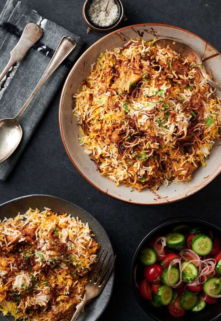 Chicken biryani table scene. Serving dish and plate of biryani from above.