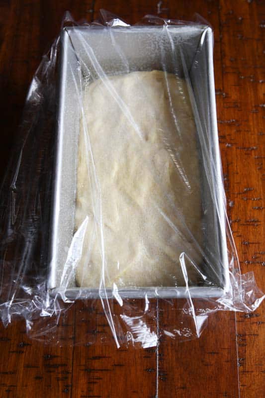 Gluten-free bread dough in loaf pan covered with plastic wrap.