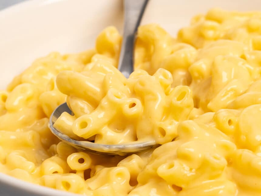 closeup image of elbow macaroni in yellow cheese sauce with metal spoon