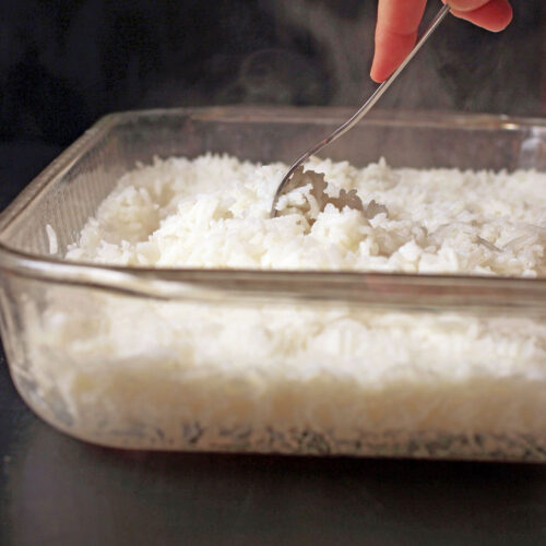 with a fork fluffing the baked rice in the pan with steam rising.