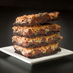 stack of four chocolate coconut bars on a square white plate.