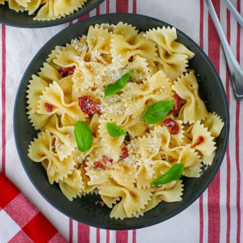 overhead shot of a bowl of brie and tomato pasta on red and white cloth.