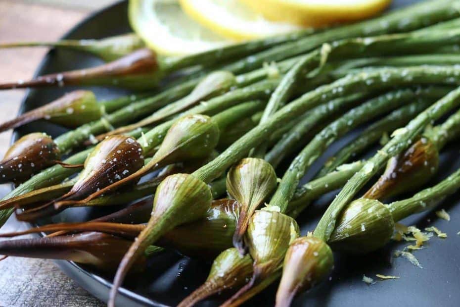 Air Fried Garlic Scapes on a black plate with lemon and lemon zest