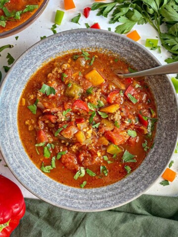 Two bowls of Stuffed Bell Pepper Soup with bell peppers and parsley scattered around the bowls.