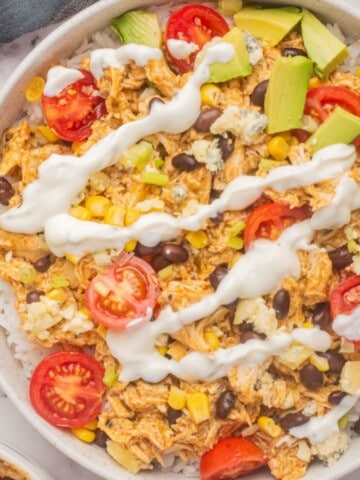 Shredded buffalo chicken rice bowl topped with colorful veggies and ranch dressing.