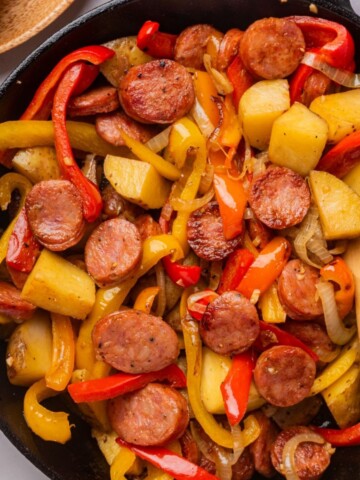 Sausage Skillet with Onions, Peppers, and Potatoes in a cast iron skillet with wooden spoon.