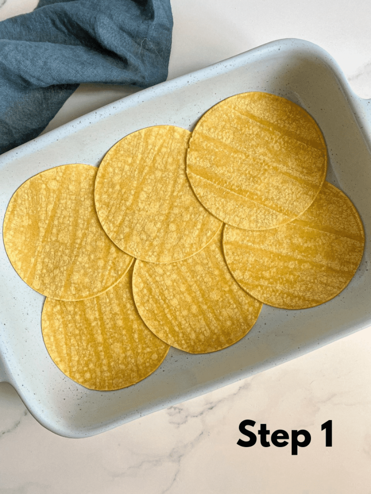 A layer of corn tortillas in the bottom of a large baking dish. Step 1 of layering the chicken casserole.