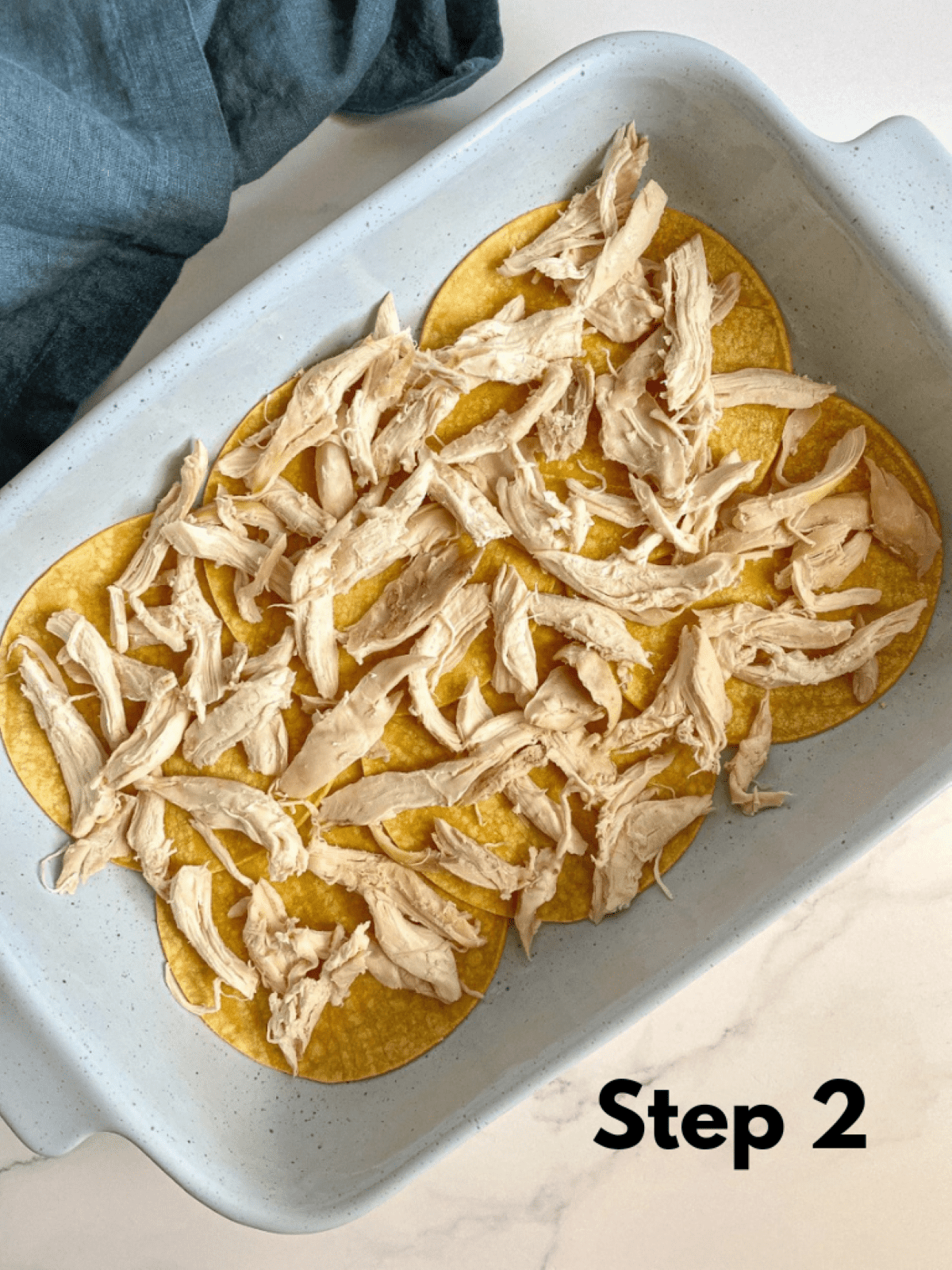 A layer of shredded chicken over corn tortillas in a casserole dish. Step 2 of layering the chicken casserole.