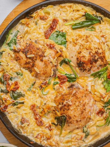 Baked chicken and orzo pasta in a skillet with spinach, artichoke hearts, and sun-dried tomatoes.