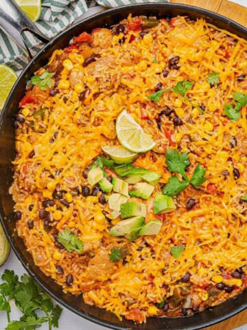 Cheesy Mexican chicken and rice in a skillet with diced avocado and lime wedge.