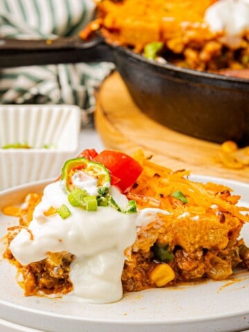 A slice of Jiffy tamale pie with cornbread crust topped with sour cream on a plate.