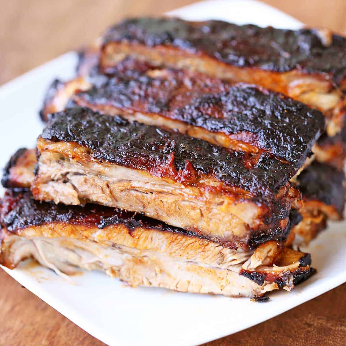 Oven baked ribs are stacked on a white plate.