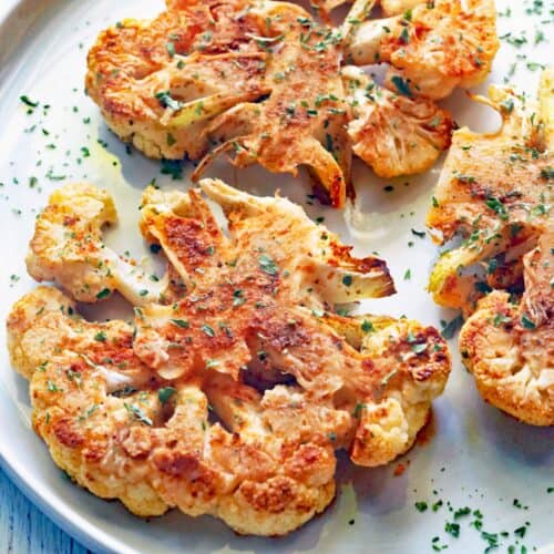 A cauliflower steak is served on a white plate.