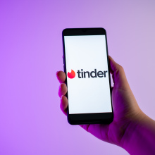 A person is holding a mobile phone with the Tinder dating app logo on its screen