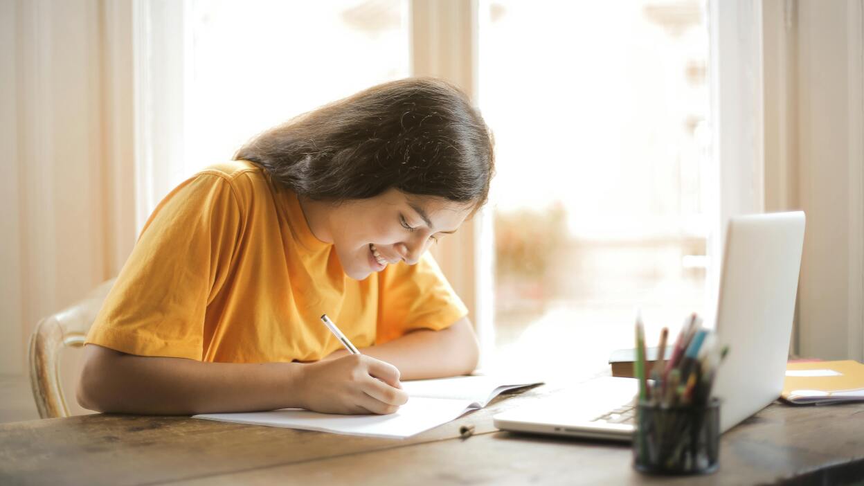 Girl writing in front of laptop