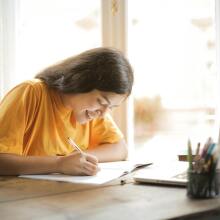 Girl writing in front of laptop