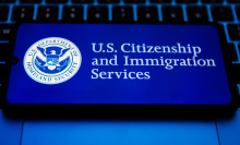 A cell phone displaying the US citizenship and immigration services logo rests on a keyboard.