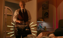 A man standing in a bedroom holding a gift basket.