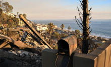 A metal mailbox sits open in front of the ruins of a home in Malibu. 