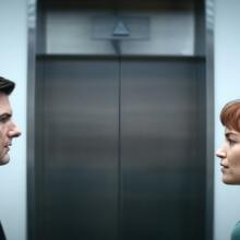 A man and a woman facing each other in front of an elevator.