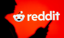 person looking at a smartphone with a Reddit logo displayed in the background