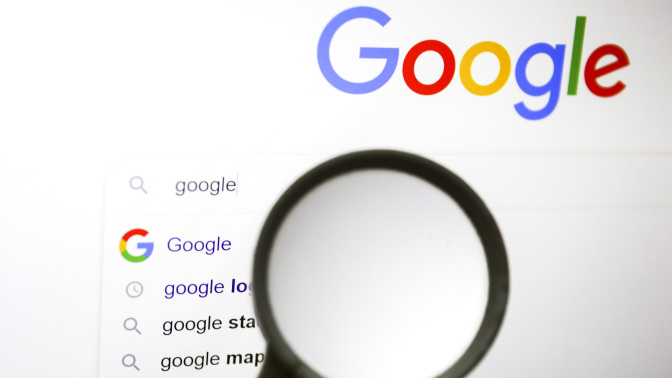 A magnifying glass is held up to a screen showing the Google homepage.