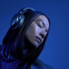 woman wearing lunar blue bose qc ultra headphones on a blue background