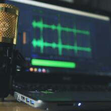 a condenser microphone next to a laptop with audio editing software