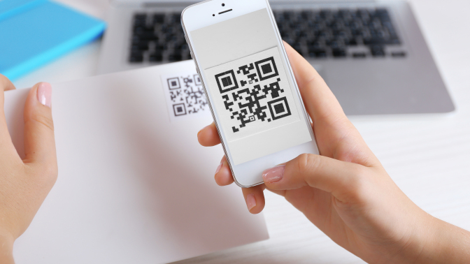 QR code on a piece of paper with person scanning it on their phone