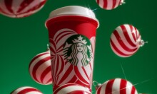 a starbucks reusable red cup covered in a design of white peppermint ornaments against a green background with ornaments surrounding it