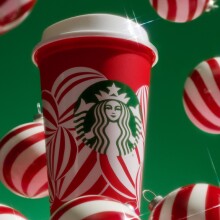 a starbucks reusable red cup covered in a design of white peppermint ornaments against a green background with ornaments surrounding it