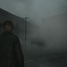 A person with short hair, wearing a dark coat, is standing on a foggy, deserted street. The atmosphere is eerie, with thick mist obscuring much of the surroundings, including power lines and dimly visible buildings in the background. The scene evokes a sense of isolation and tension