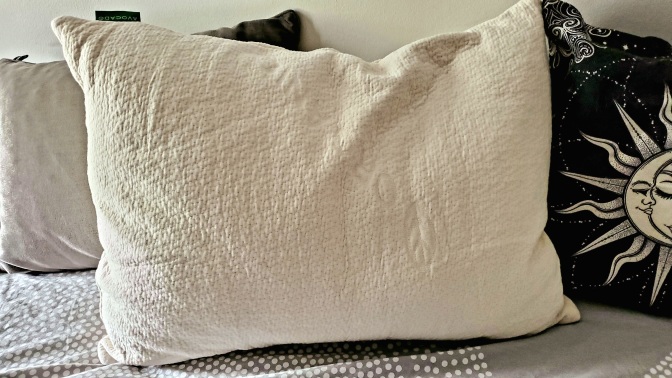 cream-colored pillow on a bed with other pillows