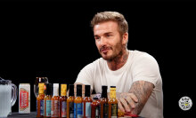 A man sits at a table covered with hot sauce in a dark room.