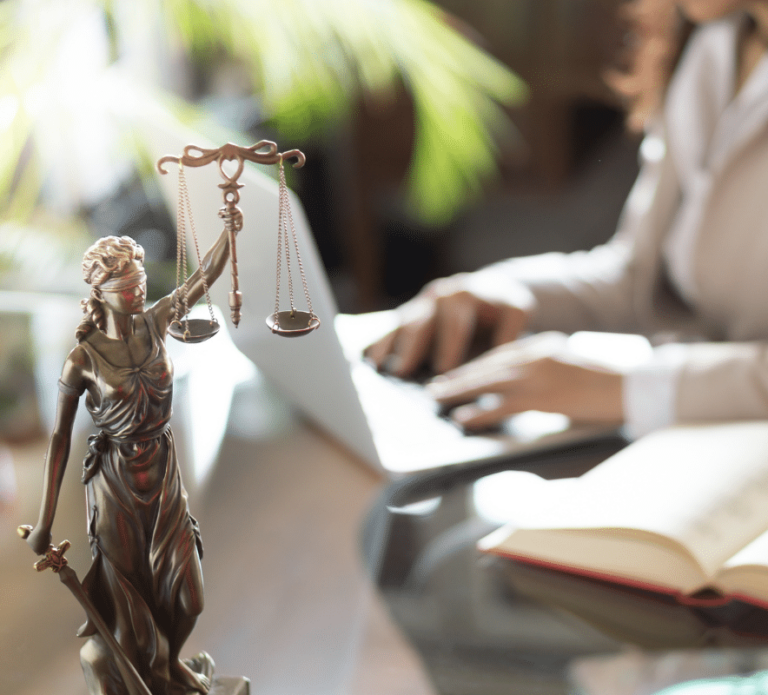 Lady of justice statute on desk with woman typing on a laptop