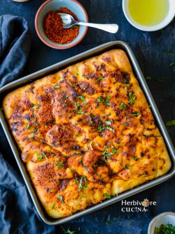 A tray filled with achari focaccia and some koro sambhar and oil on the side.