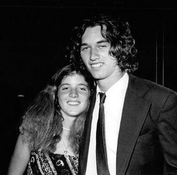 caroline kennedy and robert f kennedy jr smile and hug while posing for a photo, she wears a patterned dress, he wears a suit jacket, collared shirt and tie