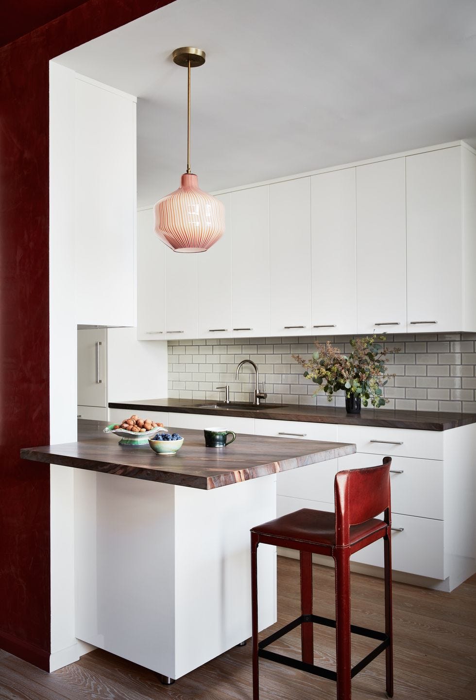 a kitchen with a white subway tile backsplash and a bold bar stool, with flowers and staged food on the counter