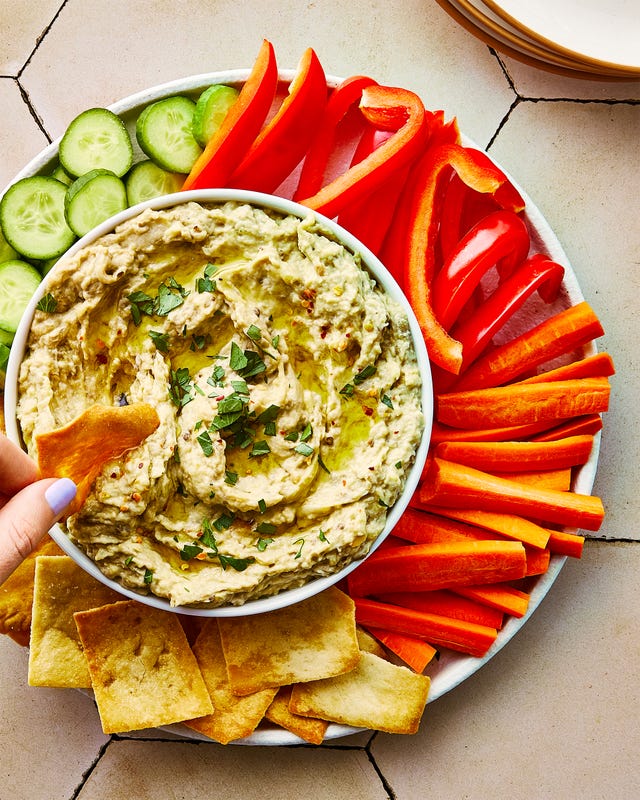 baba ganoush in a bowl topped with red pepper flakes and chopped parsley, and surrounded by pita chips and crudite