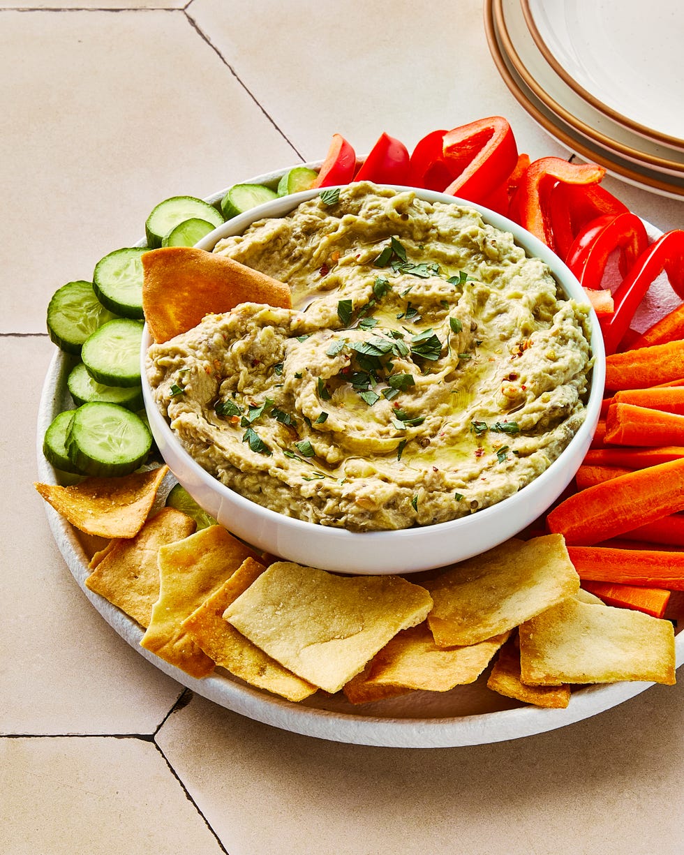 baba ganoush in a bowl topped with red pepper flakes and chopped parsley, and surrounded by pita chips and crudite