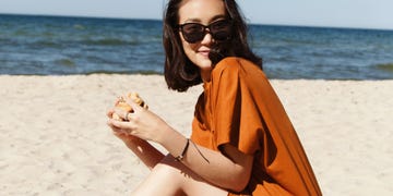 woman in sunglasses eating a burger on the beach